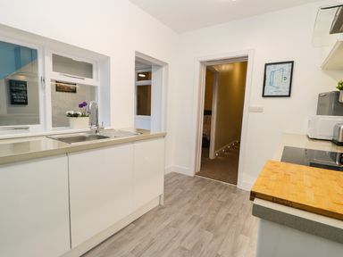 A kitchen with a sink a countertop a cutting board a microwave and a doorway leading to a hallway at Sailors Lodge in Filey