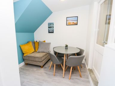 A small dining area with a round table four chairs a corner sofa with cushions and wall art at Sailors Lodge in Filey