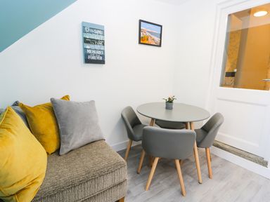 A small dining area with a round table and four chairs next to a sofa with cushions and two wall decorations at Sailors Lodge in Filey