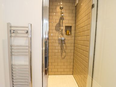 A shower area with beige subway tiles and a chrome showerhead next to a chrome towel radiator at Sailors Lodge in Filey