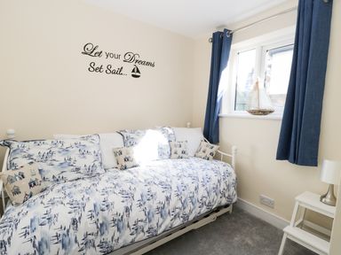 A small bedroom with a daybed with patterned bedding and cushions and a side table with a lamp at Sailors Lodge in Filey