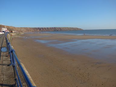 A sandy beach with a blue railing along a promenade and cliffs in the background at Sailors Lodge in Filey