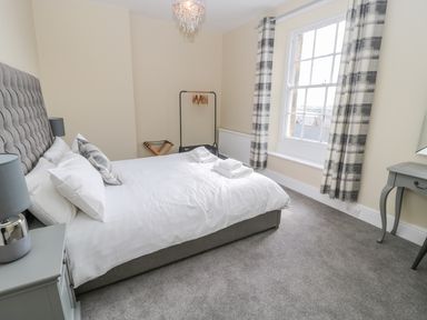 A bedroom with a double bed bedside tables lamps checked curtains and a window at Coquet View Apartment in Warkworth