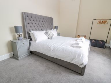 A bedroom with a gray upholstered bed with white linens and pillows beside a gray nightstand with a lamp at Coquet View Apartment in Warkworth