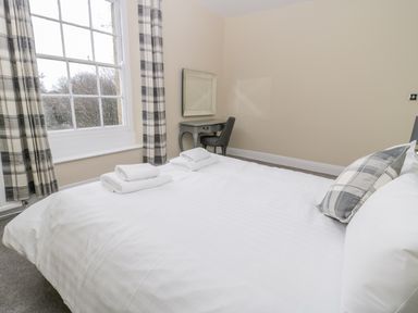 A bedroom with a bed folded towels a side table a chair a wall mirror and a window with plaid curtains at Coquet View Apartment in Warkworth