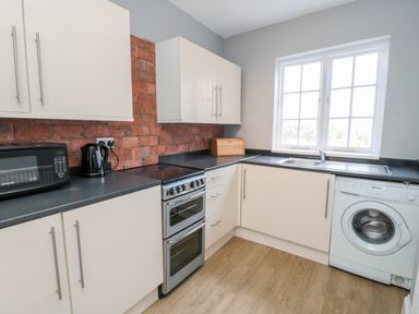 A kitchen with white cabinets a washing machine a microwave kettle stove and a window at Coquet View Apartment in Warkworth