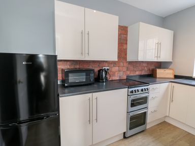 A kitchen with a black refrigerator microwave kettle stove white cabinets and a bread box at Coquet View Apartment in Warkworth