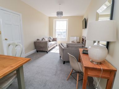 A living room with sofas a wooden desk with lamp a chair a window and a dining table at Coquet View Apartment in Warkworth