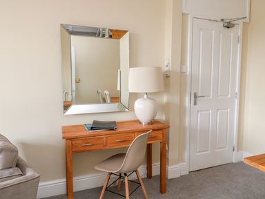 A wooden desk with a white lamp and chair in front of a wall mirror beside a white door at Coquet View Apartment in Warkworth
