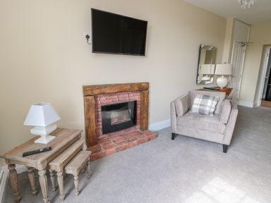 A living room with a grey armchair a brick fireplace and nested wooden side tables at Coquet View Apartment in Warkworth