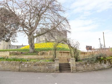 Stone steps leading to a garden area with a large tree and yellow flowers on a grassy mound with a stone building in the background at Coquet View Apartment in Warkworth