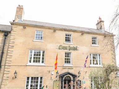 The front facade of the Sun Hotel with multiple windows and entrance under a small black canopy with flags at Coquet View Apartment in Warkworth