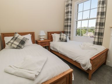 A bedroom with two single beds a nightstand with a lamp and a window with plaid curtains at Coquet View Apartment in Warkworth