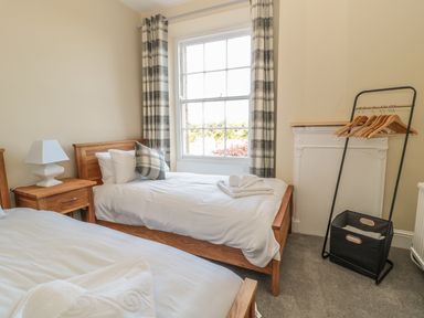 A bedroom with two single beds a wooden nightstand a window with plaid curtains and a clothes rack at Coquet View Apartment in Warkworth