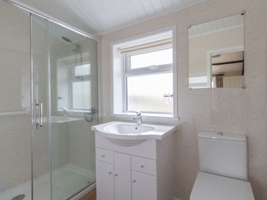 A bathroom with a glass shower enclosure a sink with cabinet below a window a mirror and a toilet at Village View in Burton Bradstock