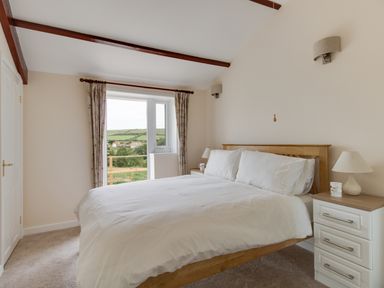 A bedroom with a wooden bed and bedside tables near a window with curtains at Village View Burton Bradstock