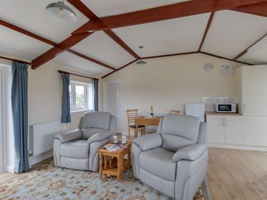A living room with two armchairs a small wooden table a dining table and kitchenette at Village View in Burton Bradstock