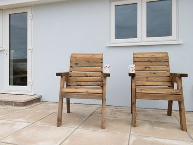 Two wooden chairs with mugs on the armrests outside a house with a door and window at Village View Burton Bradstock