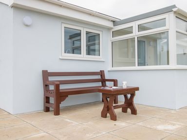 An outdoor patio with a wooden bench and table against a white house at Village View in Burton Bradstock