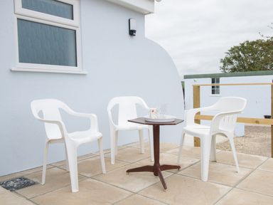 An outdoor patio area with three white plastic chairs around a small wooden table with a tray and cups at Village View in Burton Bradstock