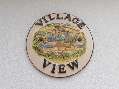 A round plaque with a village scene and the words Village View on a textured wall at Village View in Burton Bradstock