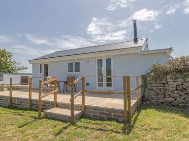 A small white house with a wooden deck and steps in a grassy yard at Village View in Burton Bradstock