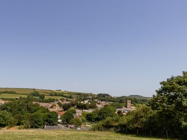 A village with houses trees and a church tower surrounded by fields at Village View in Burton Bradstock