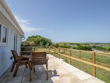 An outdoor patio with wooden chairs and table overlooking a grassy landscape at Village View in Burton Bradstock
