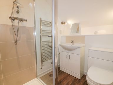 A bathroom with a shower, sink with cabinet, toilet, heated towel rail, and a small mirror at Lily Cottage in Camelford