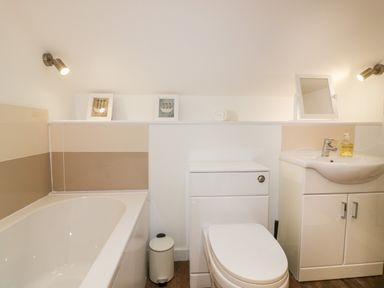 A bathroom with a bathtub toilet sink mirror and framed pictures at Lily Cottage in Camelford