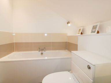 A bathroom with a bathtub a toilet and two framed pictures on a shelf at Lily Cottage in Camelford