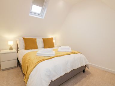 A bedroom with a double bed yellow cushions and blanket bedside tables with lamps at Lily Cottage in Camelford