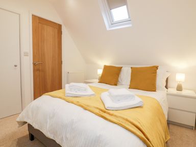 A bedroom with a bed with yellow cushions and blanket towels on top and two bedside tables with lamps at Lily Cottage in Camelford