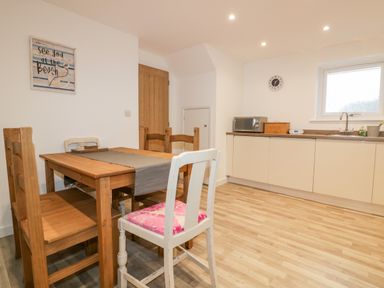 A kitchen with wooden dining table and chairs a microwave on the counter and a window at Lily Cottage in Camelford