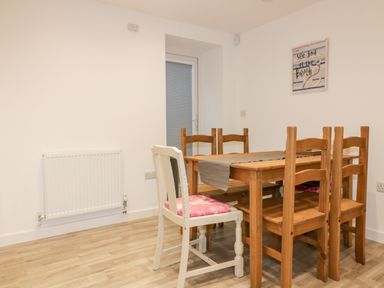 A dining area with a wooden table and five chairs including one white chair with a pink cushion at Lily Cottage in Camelford