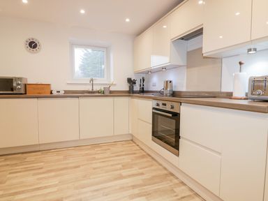 A kitchen with white cabinets a window a microwave a bread box and an oven at Lily Cottage in Camelford