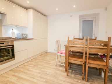 A kitchen with white cabinets an oven a toaster a wooden dining table and chairs at Lily Cottage in Camelford