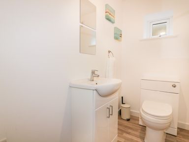 A bathroom with a sink, toilet, small window, and two pictures on the wall at Lily Cottage in Camelford