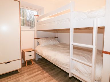 A bedroom with white bunk beds a wardrobe and a bedside table at Lily Cottage in Camelford