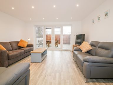 A living room with two sofas a coffee table a television and glass doors looking out to a patio at Lily Cottage in Camelford