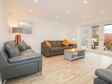 A living room with sofas coffee table lamp and glass doors opening to a garden at Lily Cottage in Camelford