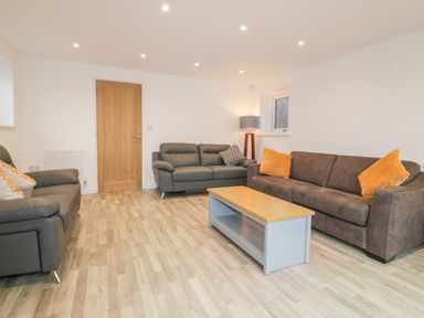 A living room with three sofas a wooden coffee table a floor lamp and a wooden door at Lily Cottage in Camelford