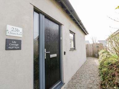 A black front door with address signs on a building with a gravel path alongside at Lily Cottage in Camelford