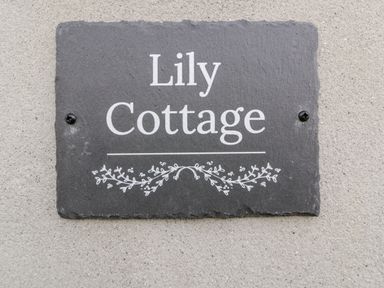 A slate house name plaque with Lily Cottage and decorative vine design