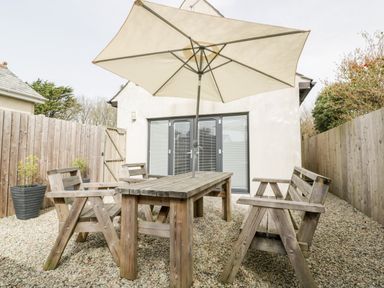An outdoor seating area with a wooden table bench chairs and a large umbrella in a gravel yard at Lily Cottage in Camelford
