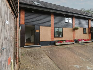 The exterior of Bantam Cottage with black and beige walls flowers in planters under the windows and an open door at Bantam Cottage in Little Woodford near Ottery St Mary