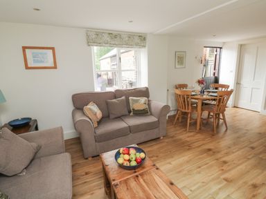 A living room with two sofas a wooden coffee table with a bowl of fruit and a dining table with four chairs at Bantam Cottage in Little Woodford near Ottery St Mary