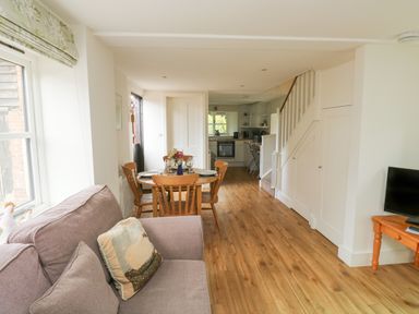 A living room with a sofa pillow dining table and chairs kitchen and TV on a wooden table at Bantam Cottage in Little Woodford near Ottery St Mary