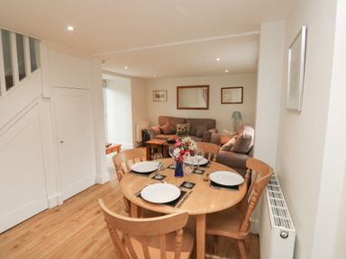 A dining area with a wooden table set for four and a living room with sofas and a coffee table at Bantam Cottage in Little Woodford near Ottery St Mary