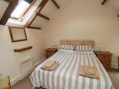 A bedroom with a double bed with striped bedding two wooden nightstands and a skylight window at Bantam Cottage in Little Woodford near Ottery St Mary